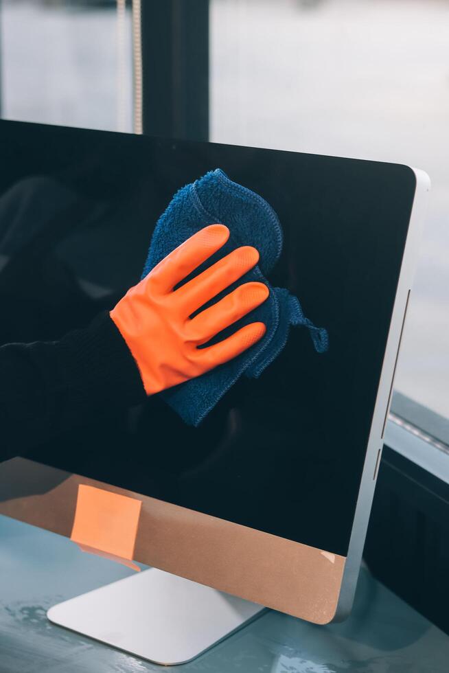 A person wearing orange gloves cleaning a computer monitor photo