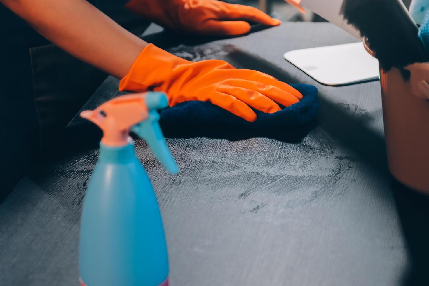 A person wearing gloves and an orange glove is cleaning a table photo