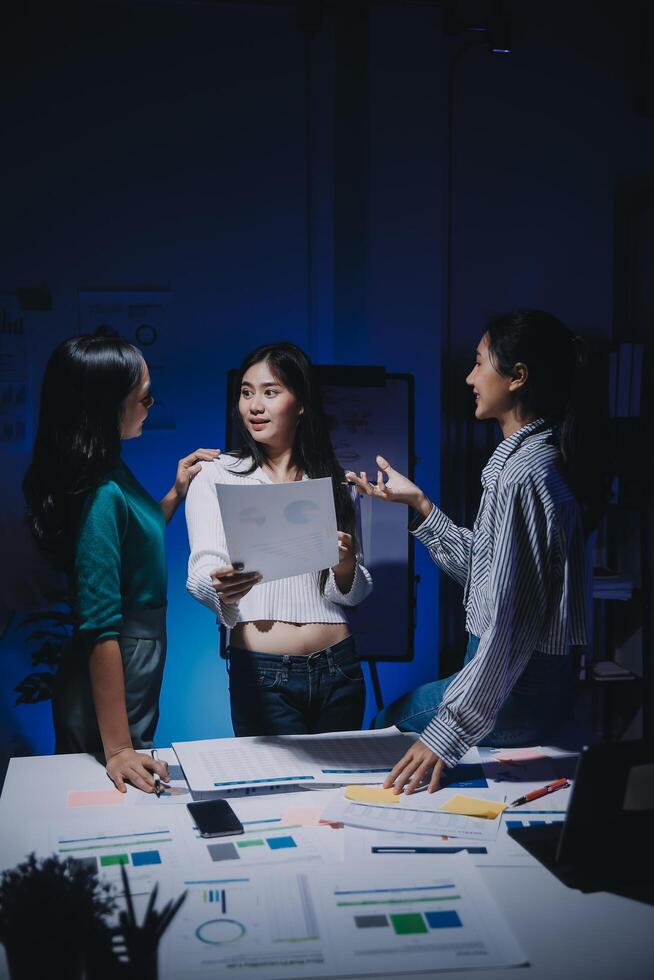 Three women standing around a table with papers photo