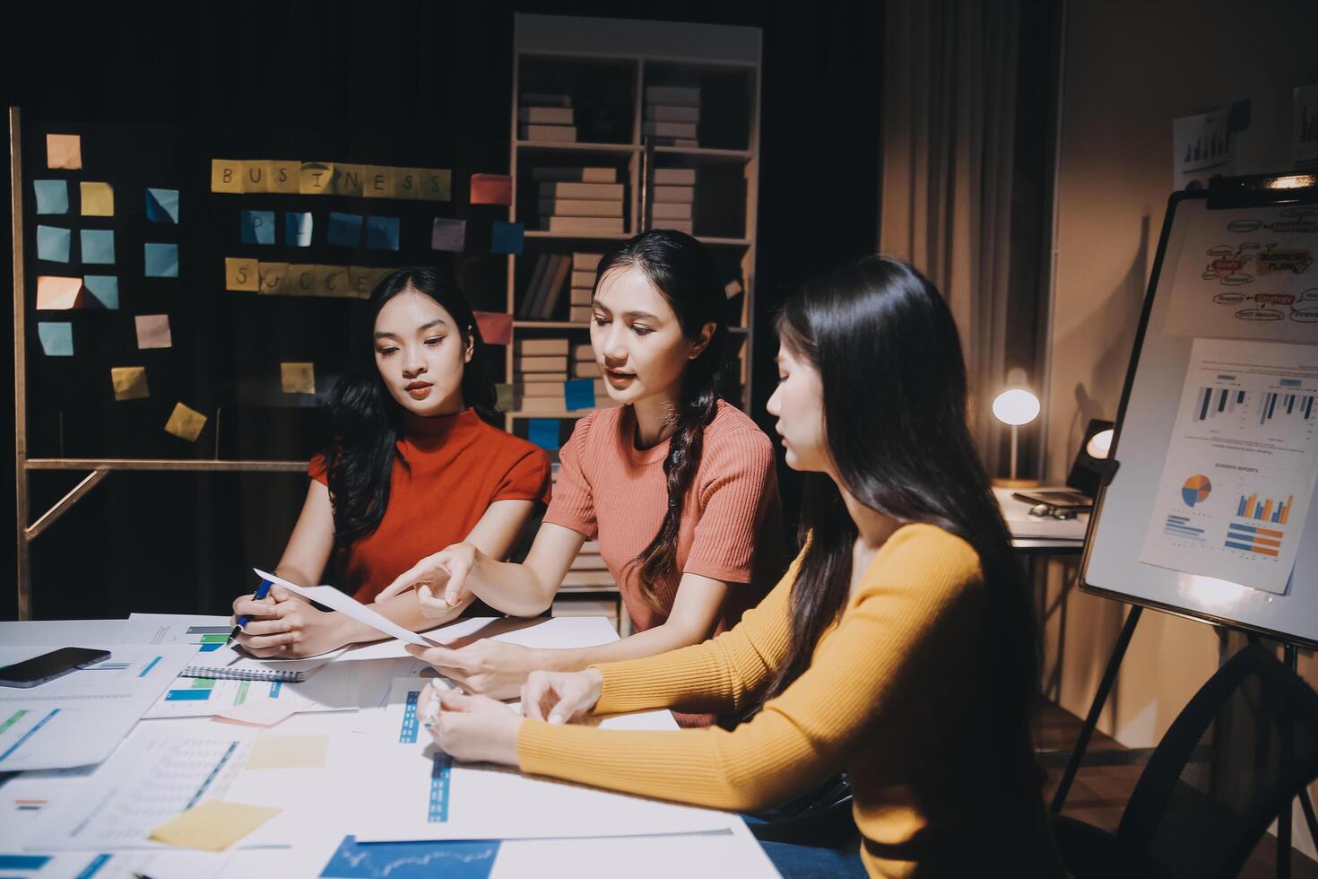 Three women sitting at a table with papers and a whiteboard photo