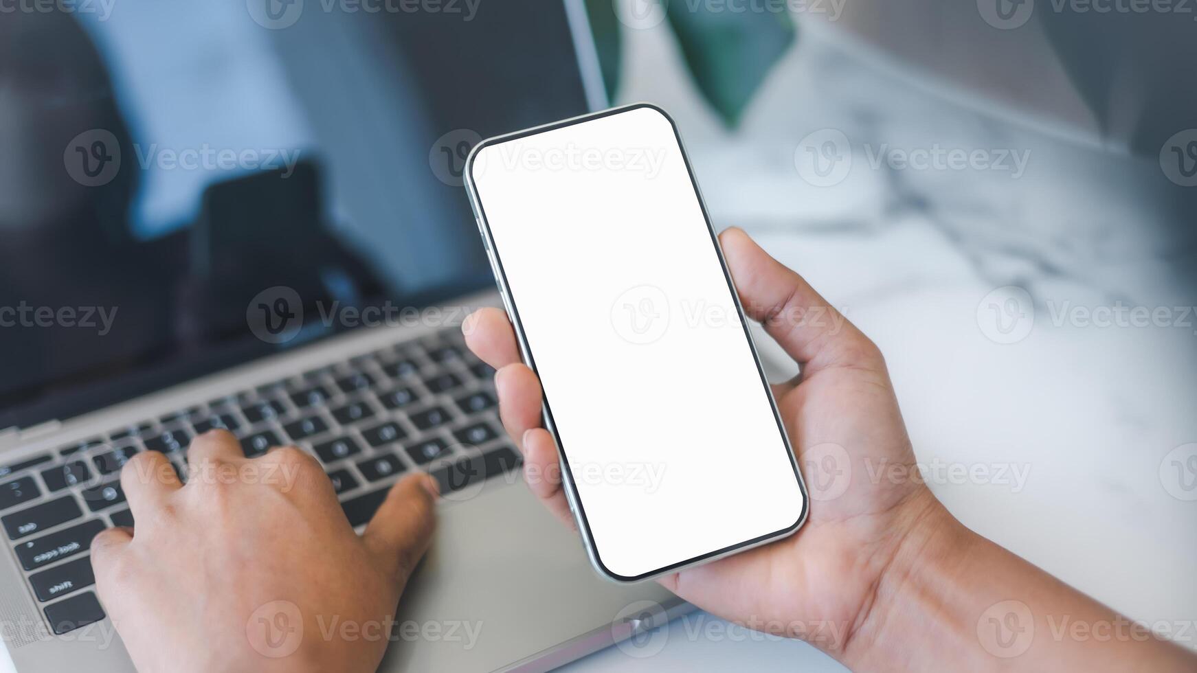 Cell phone white screen mockup, Human hand holding mobile phone with blank screen while working at coffee shop, Businessman using smartphone, Social media advertisement, Design creative work space. photo