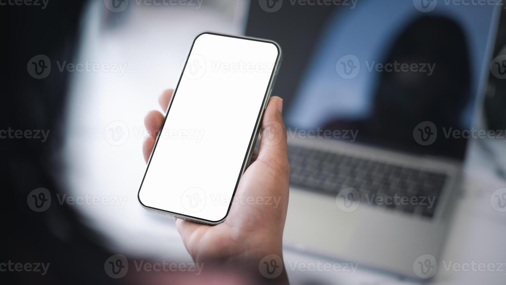 Cell phone white screen mockup, Human hand holding mobile phone with blank screen while working at office, Design creative work space, Businessman using smartphone, Social media advertisement. photo