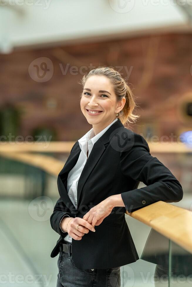 Smiling businesswoman leaning on railing in modern office building photo