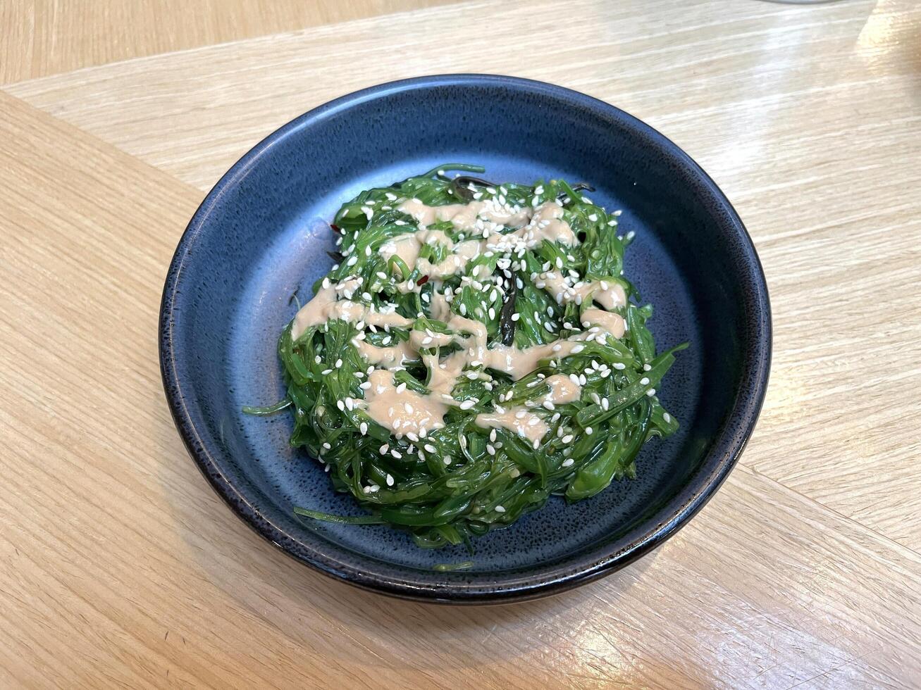 Seaweed salad in Goma Dare Sauce with sesame seeds in a ceramic bowl on Japanese restaurant table photo
