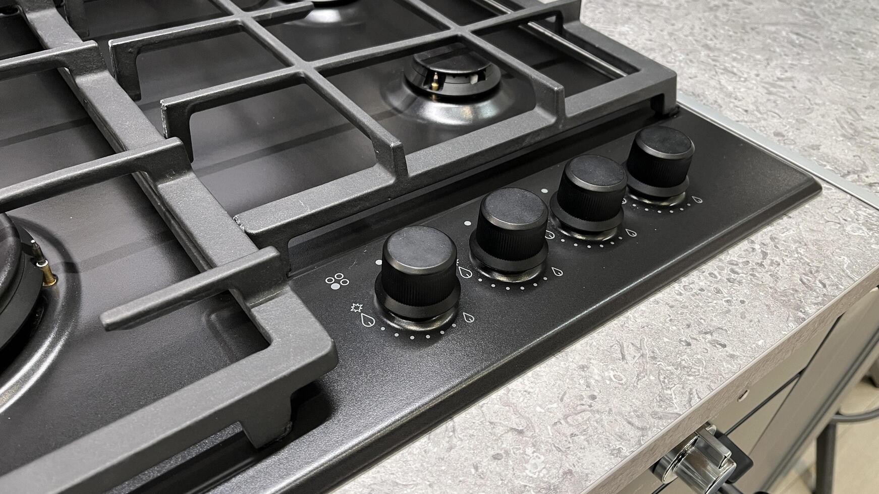 Close-up of a modern gas stovetop with multiple burners and control knobs, set against a textured countertop photo