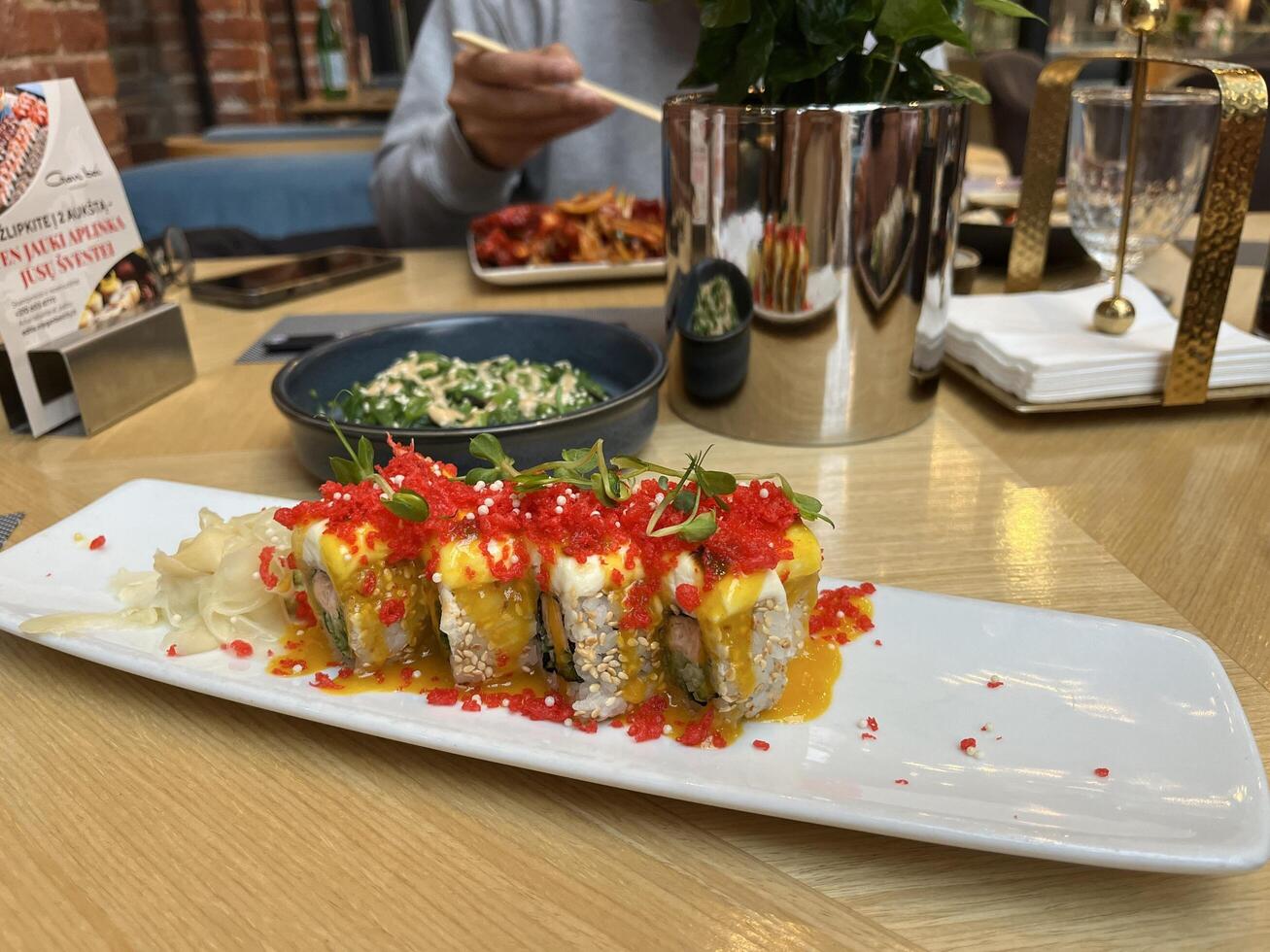 Kaunas, Lithuania. Jan 26, 2025. Japanese Restaurant table served with Red Dragon Sushi, Seaweed salad and unrecognized man enjoy the food photo