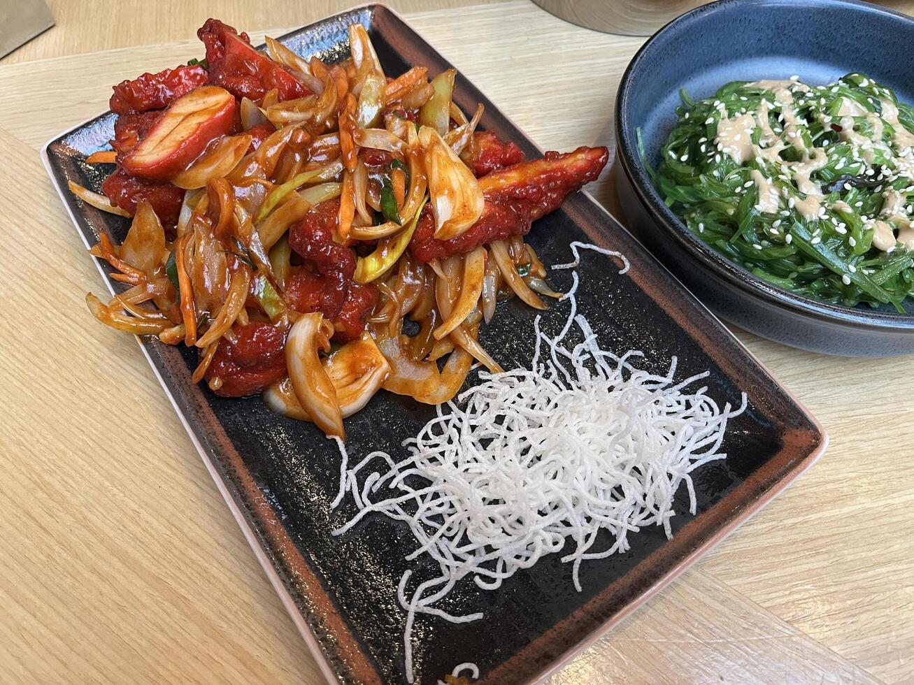 Sliced chicken fillet with hot garlic sauce with vegetables and fried glass noodle and a bowl of seaweed salad photo