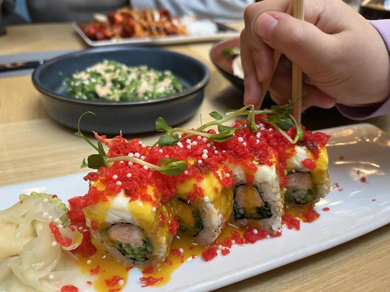 A kids hand hold chopstick take Red Dragon Sushi. Sushi with salmon, panko tiger prawns, cucumber, unagi sauce, mayonnaise, sesame seeds in Japanese restaurant photo