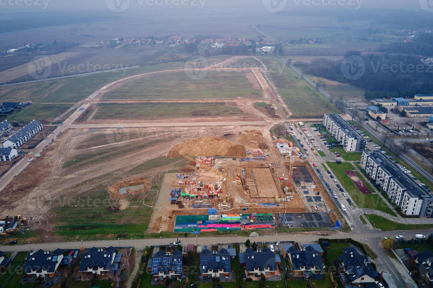 Aerial view of residential buildings under construction surrounded by completed homes and apartments. Cranes, foundations and building materials at construction site. New neighborhood in small town photo