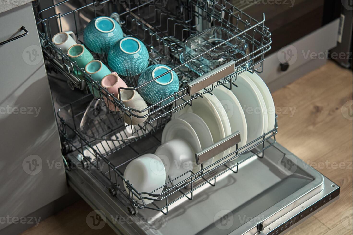 Open dishwasher in kitchen loaded clean crockery items, including white plates, bowls and cups ready for unloading. Modern home appliance photo