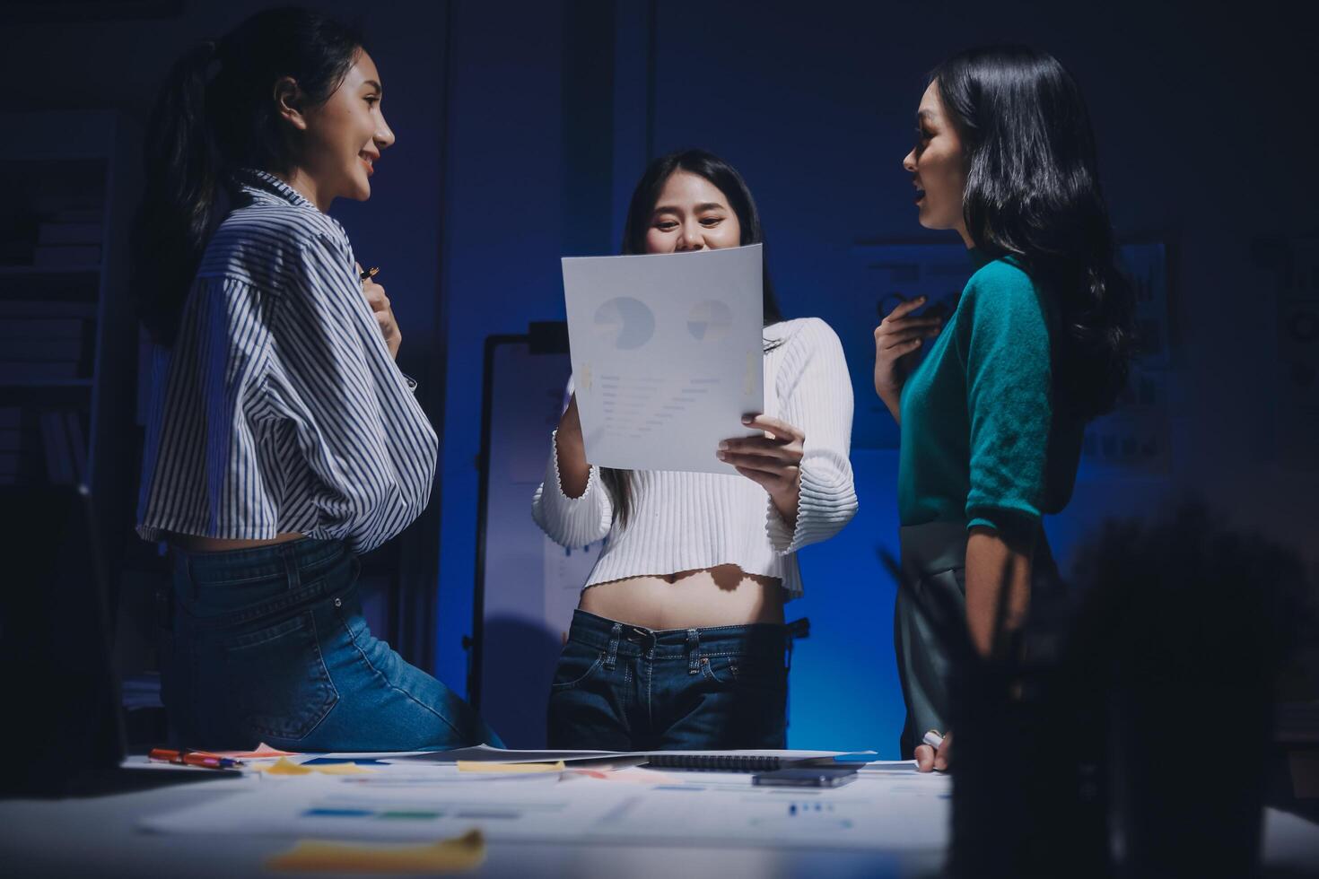 Three women standing around a table with a piece of paper photo