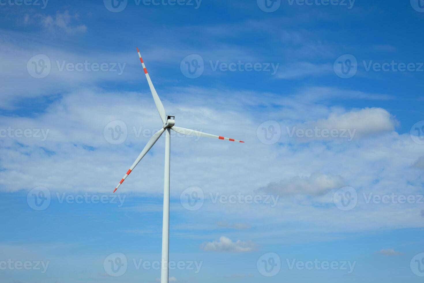 Large wind turbine spinning against a blue sky with scattered clouds in daytime photo