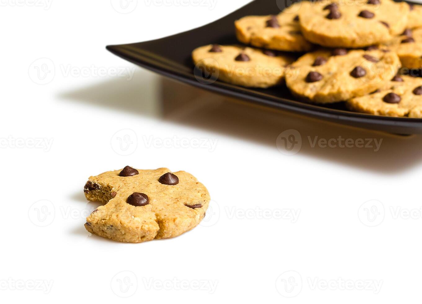 Detail of chocolate chip cookie with a bite and pile of cookies in a plate on the background photo