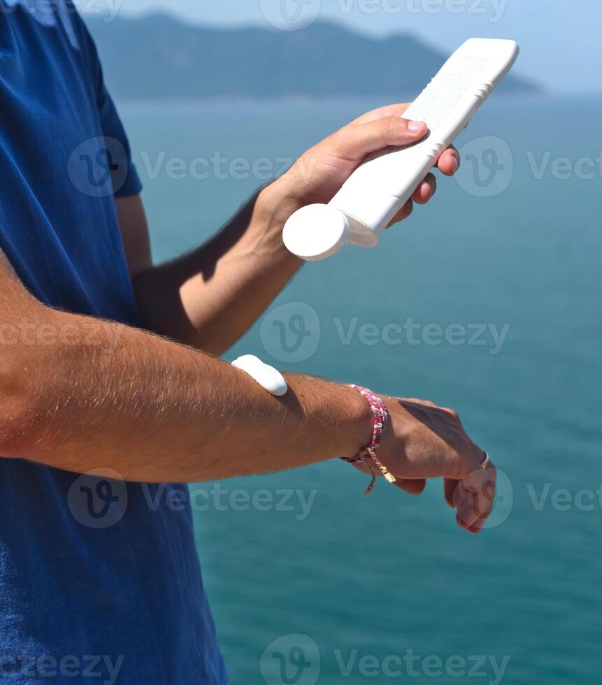 Using sunscreen cream on the arm against sea under sunlight photo
