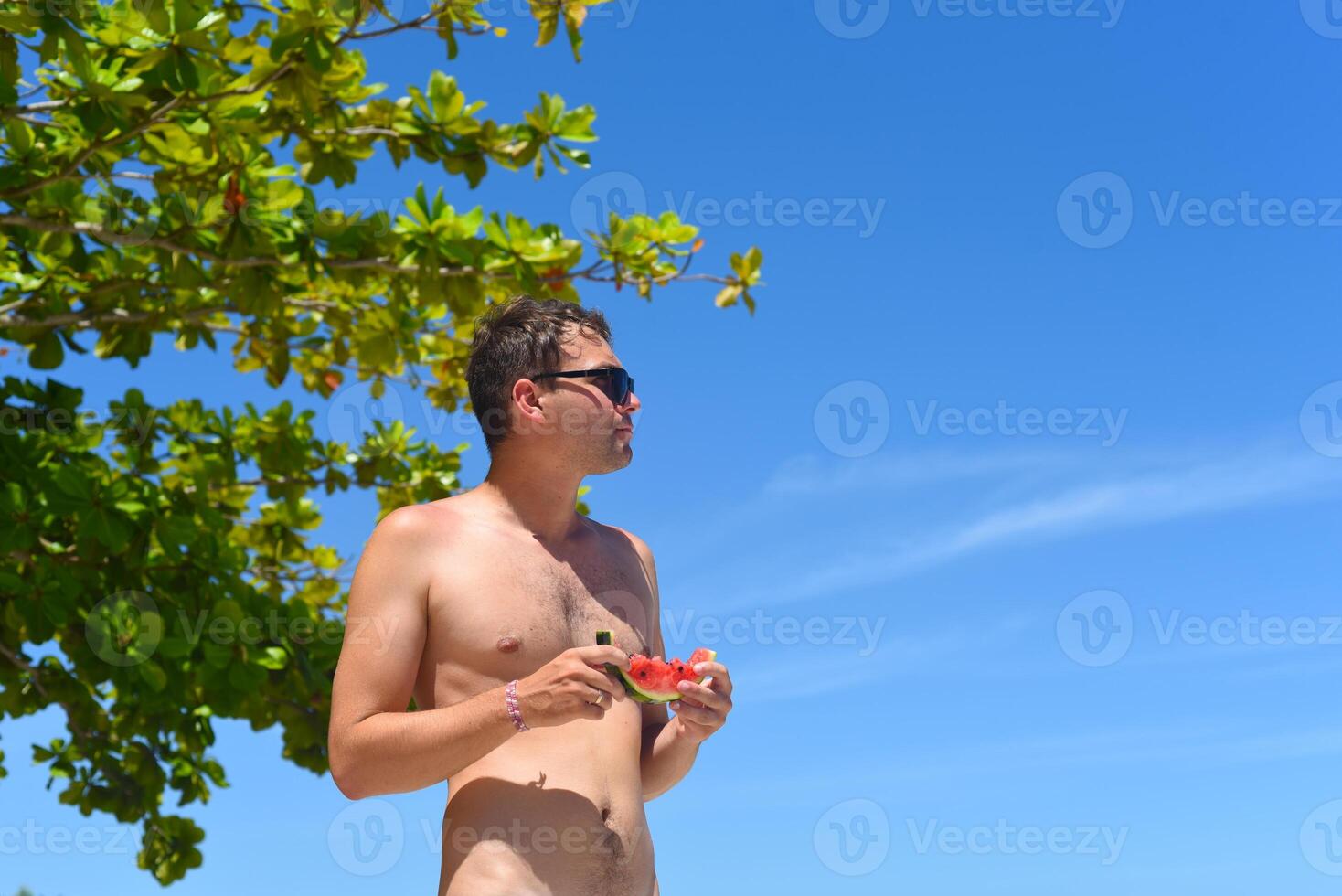Young man in sunglasses eating a watermelon on the beach photo