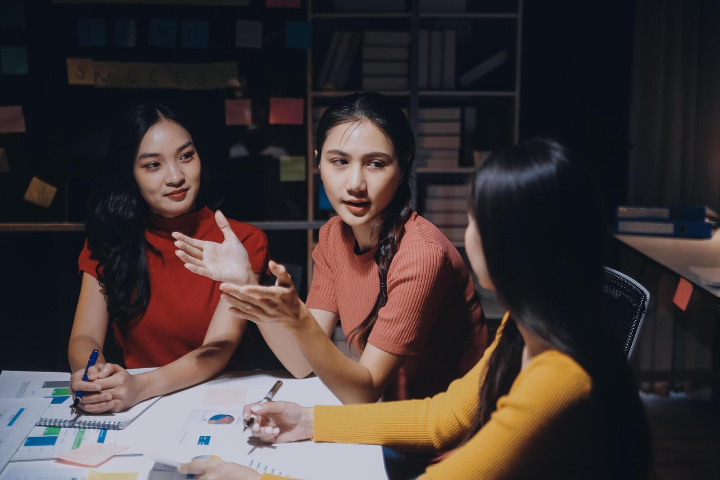 Three women sitting at a table with a whiteboard photo
