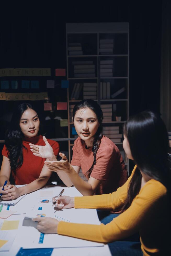 Three women sitting at a table with a whiteboard photo