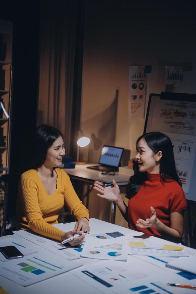 Two women sitting at a table with papers and a laptop photo