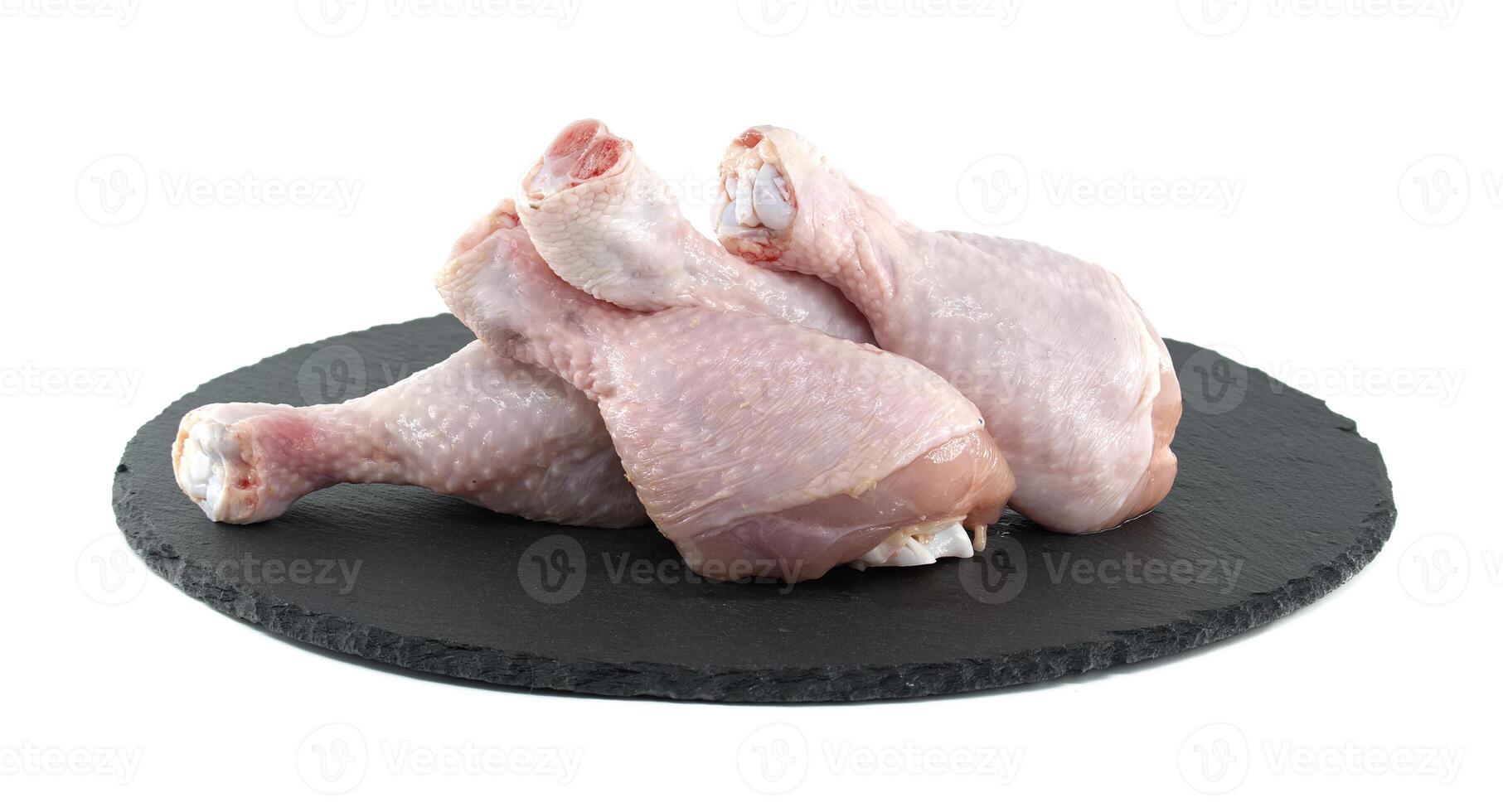 Raw chicken drumsticks resting on a black slate plate photo