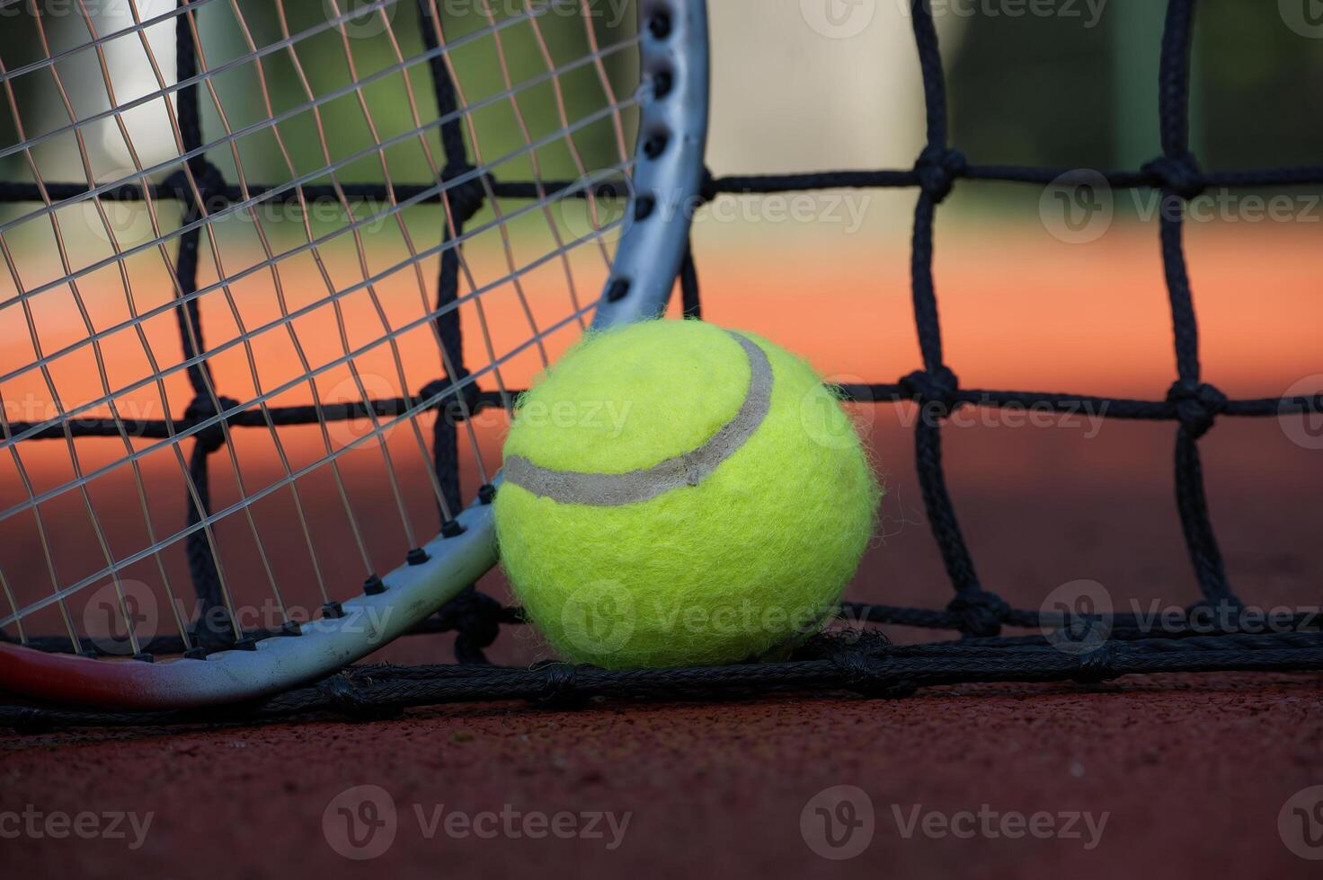 Tennis ball and racket leaning on the net of a clay court photo
