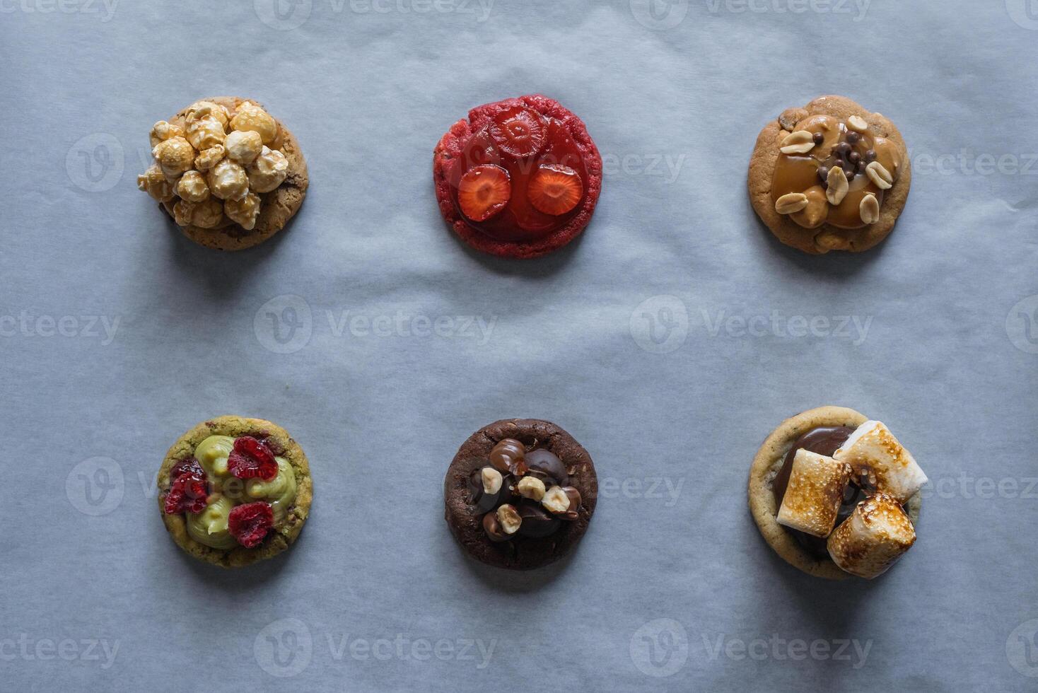 Collection of homemade cookies with different toppings - raspberry, strawberry, pistachio, caramel, chocolate, peanuts, marshmallow, popcorn flavor. photo