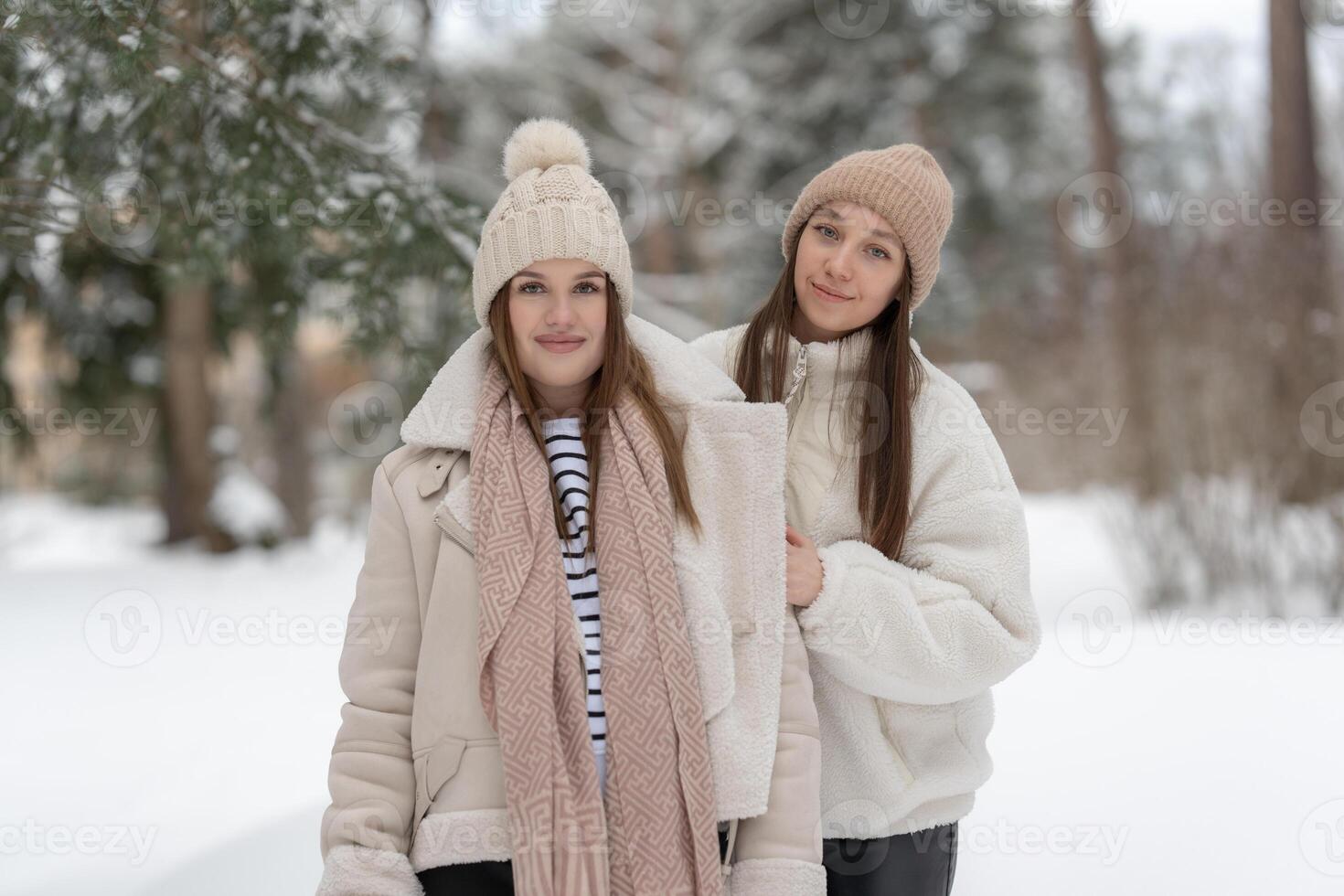 Two young women standing in a snowy park, smiling and enjoying the winter season with copy space for text. Concept of friendship, seasonal fashion, and outdoor relaxation in a serene environment. photo