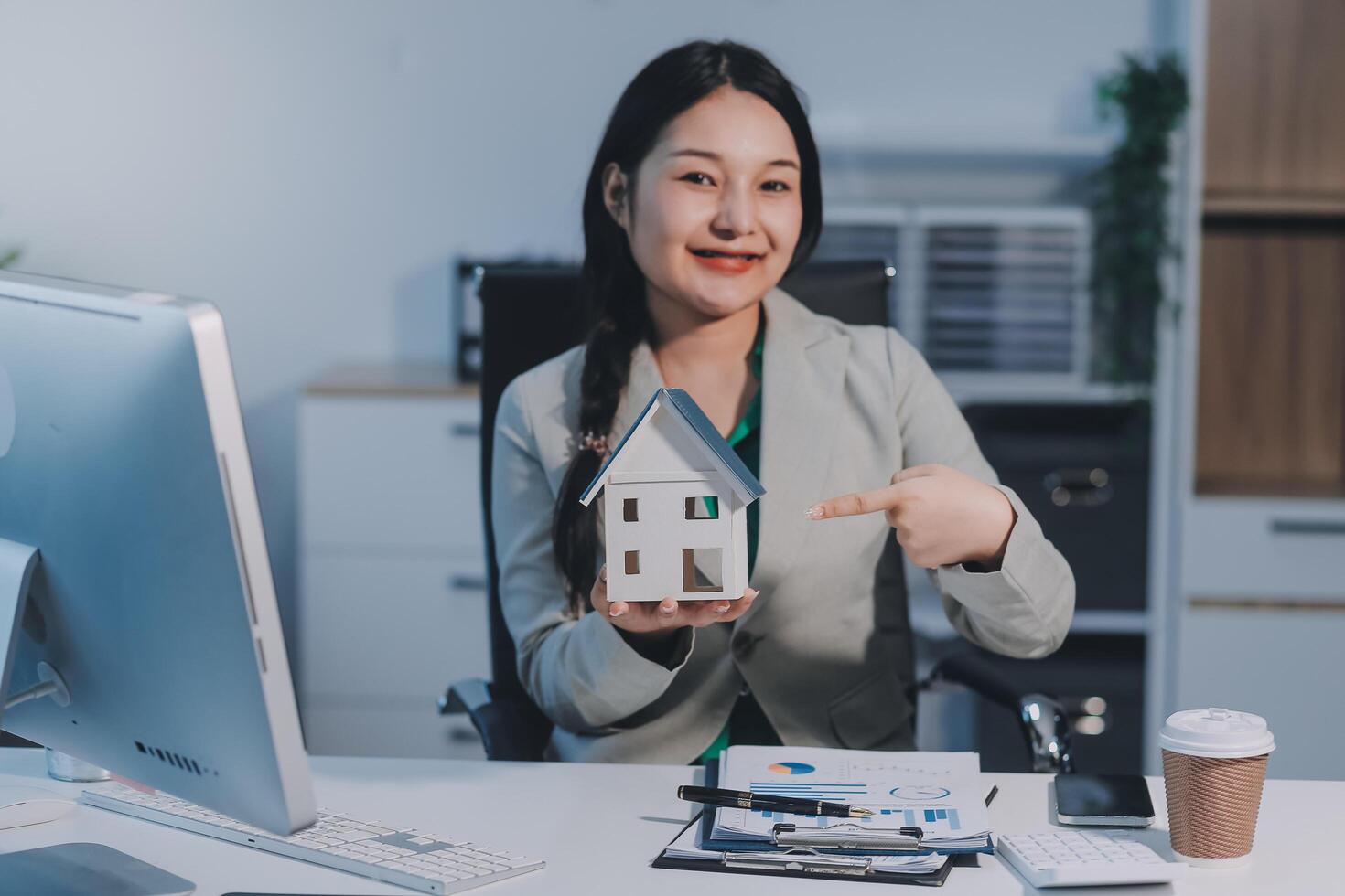 A woman holding a house model in front of her computer photo