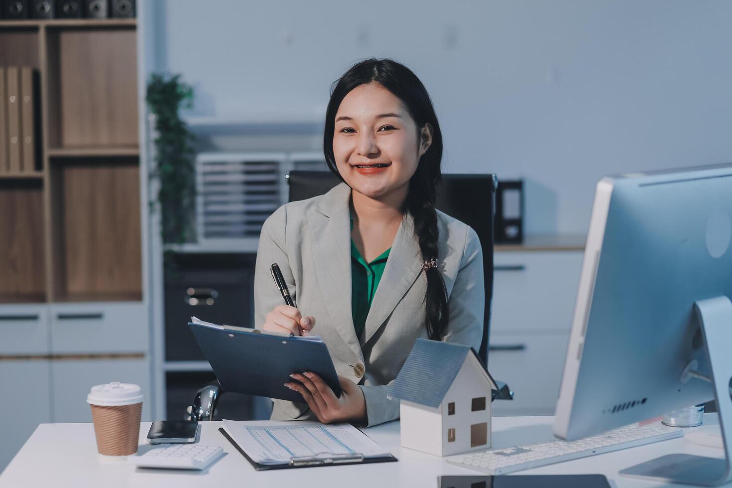 Asian woman in business suit sitting at desk with laptop and pen photo