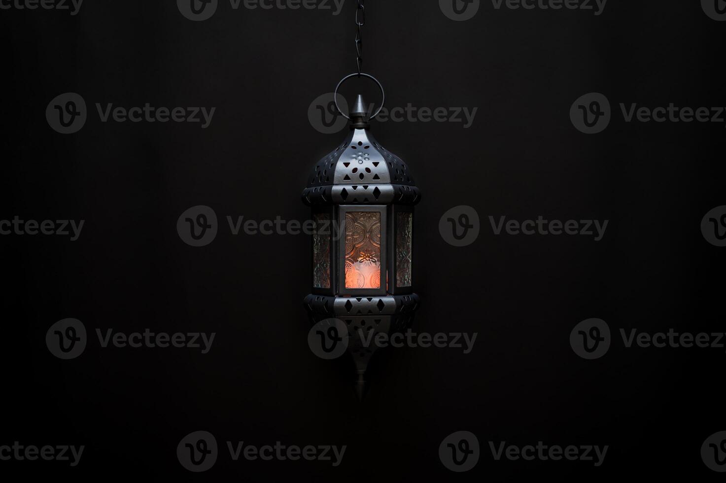 Black hanging lantern with light on dark background. photo
