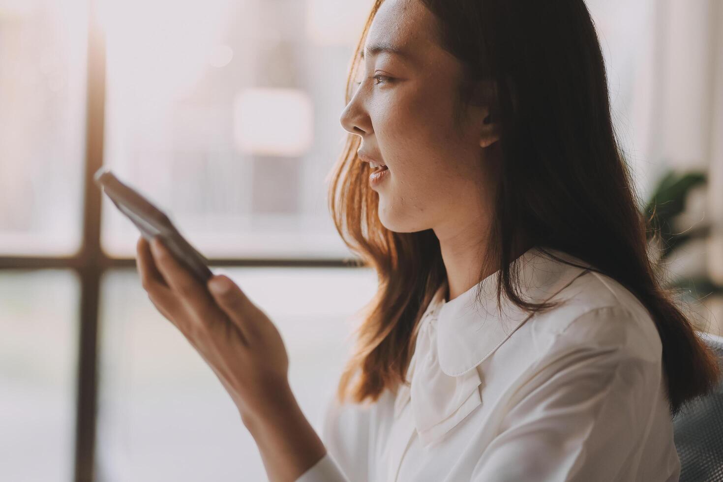 A woman is using her cell phone while sitting in front of a window photo