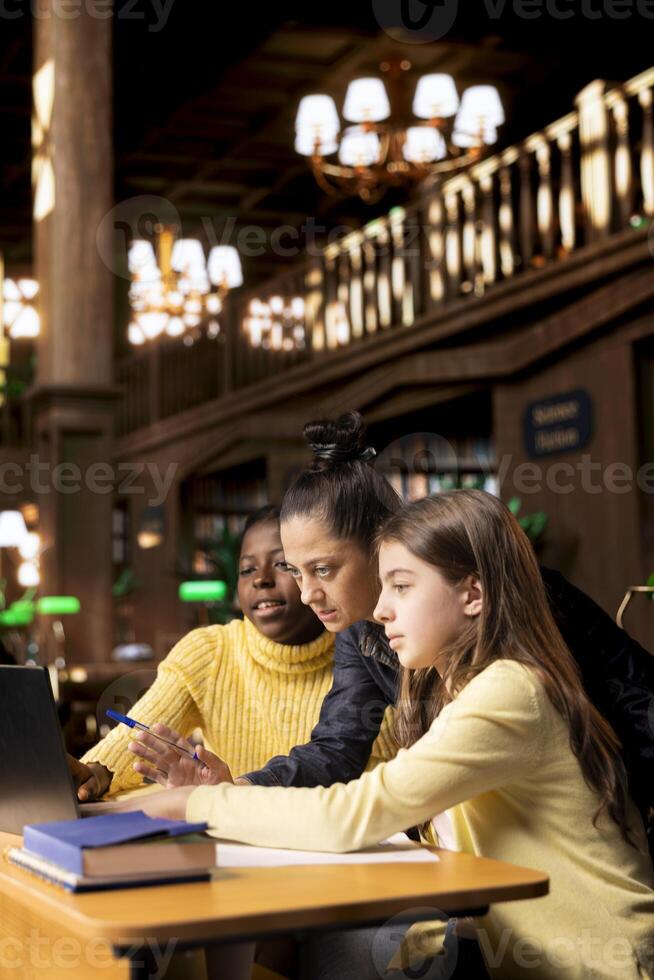 Elementary students receiving support from a tutor working on homework assignments together in a diverse learning environment in the school library. Professor guiding her pupils before class. photo