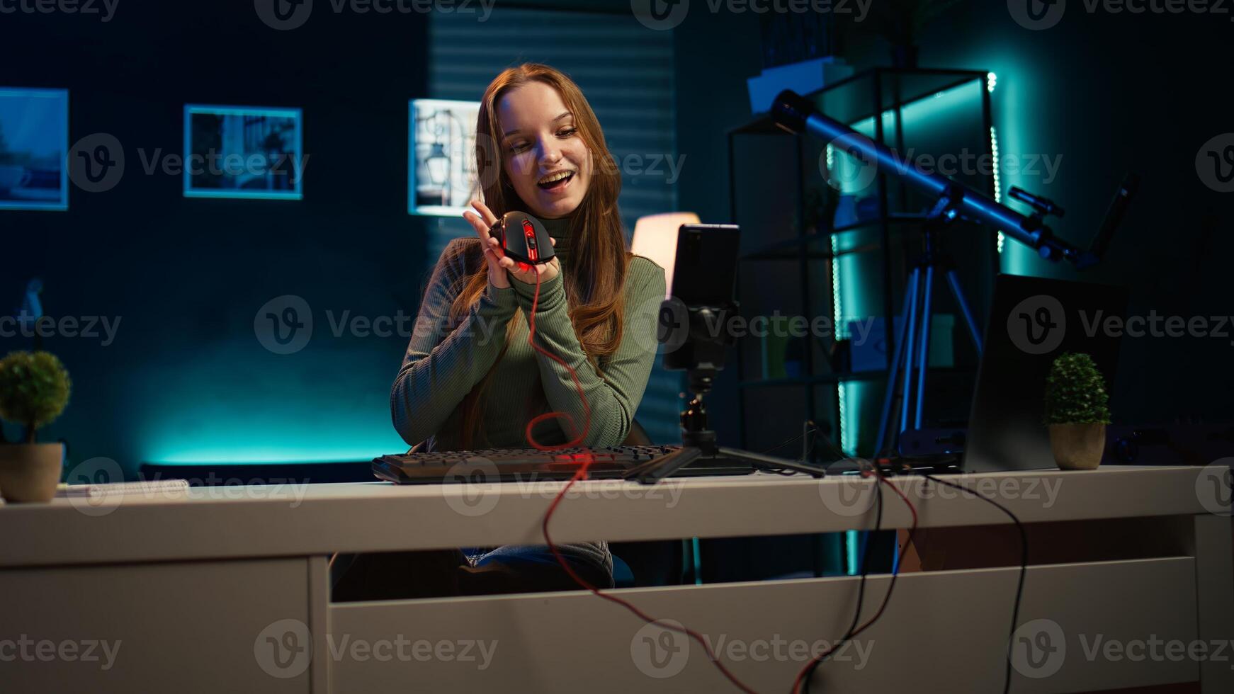 Gen Z girl presenting RGB lit mouse and keyboard while doing review in personal studio to see if price is justified. Young influencer showcasing neon lit computer peripheral features to fans, camera B photo