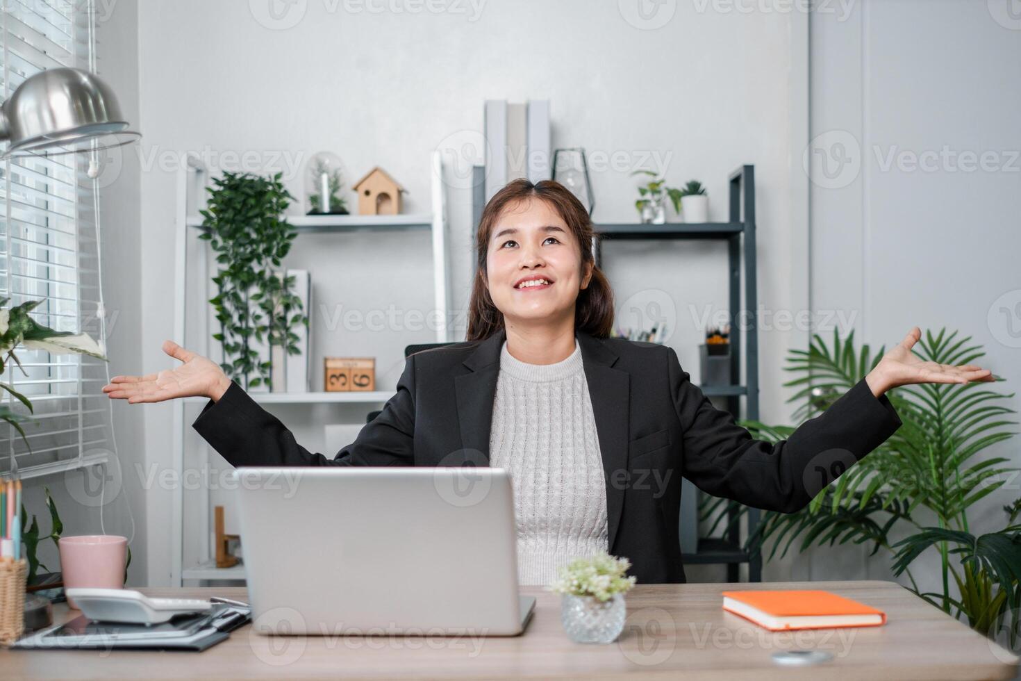 Happy businesswoman in a modern office, celebrating success with a laptop, surrounded by plants and office decor. photo