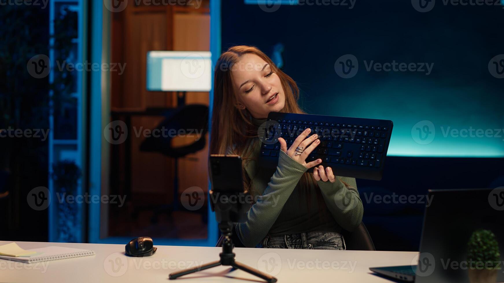 Woman presenting keyboard from brand sponsoring , advising fans to purchase it. Young online star does influencer marketing by advertising computer peripheral to fans, camera A photo