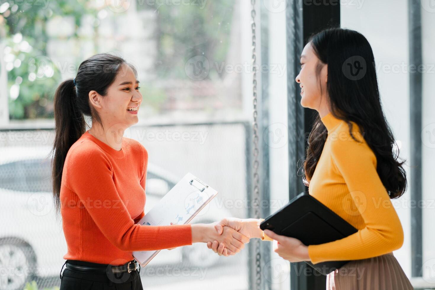 Two women in a modern office setting, shaking hands and smiling, symbolizing successful business collaboration. photo