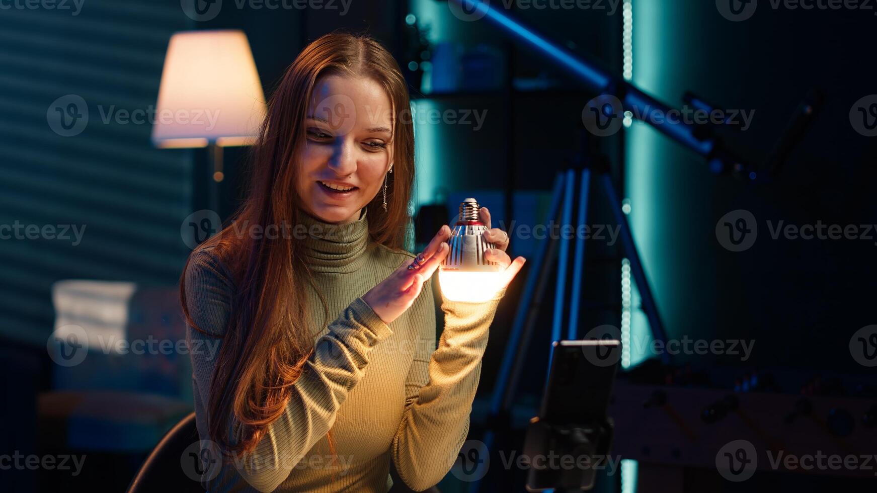 Young influencer filming review of light bulb able to change into different colors. Content creator showcasing smart home automation technology in apartment studio, camera A photo
