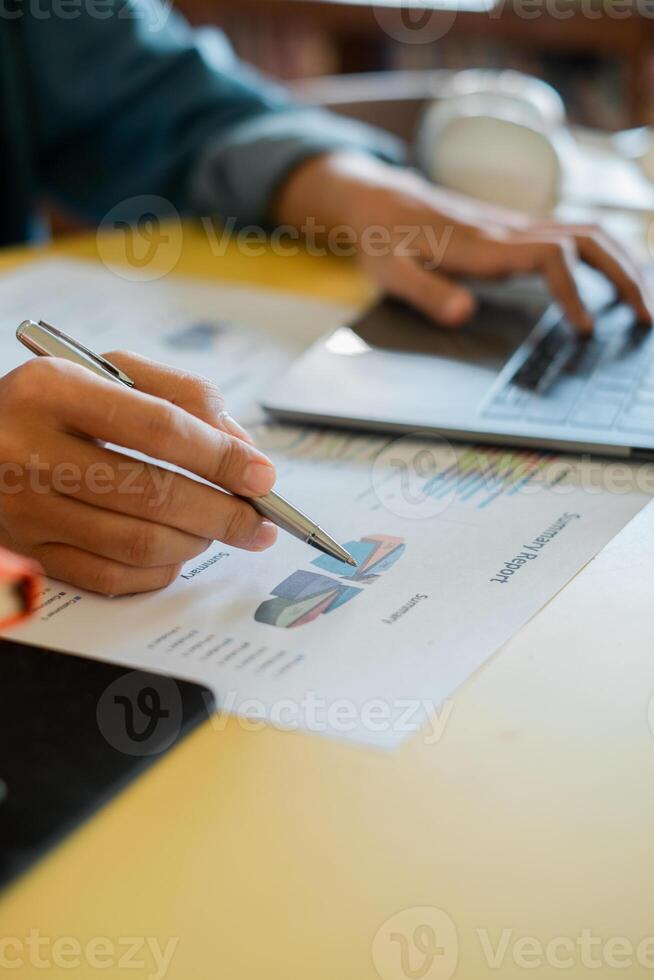 Close-up of a person working on a laptop, analyzing financial graphs and data with a pen in an office environment. photo