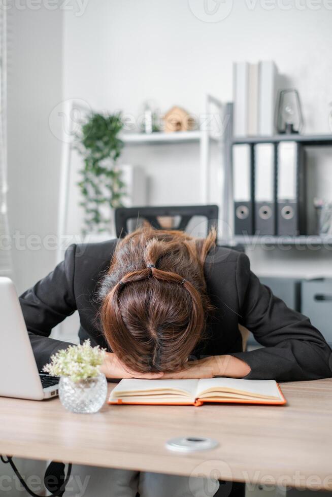 Tired businesswoman resting her head on a desk in an office setting, symbolizing stress and burnout. photo