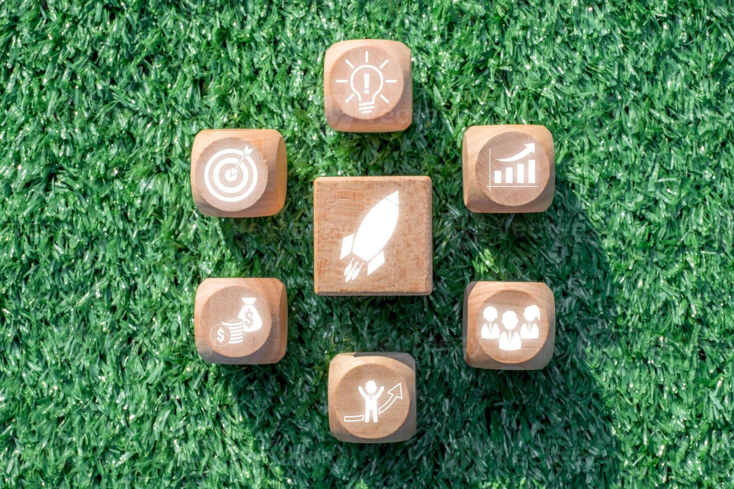 Wooden blocks with business icons symbolize startup concepts, innovation, and growth on a vibrant green grass background. photo