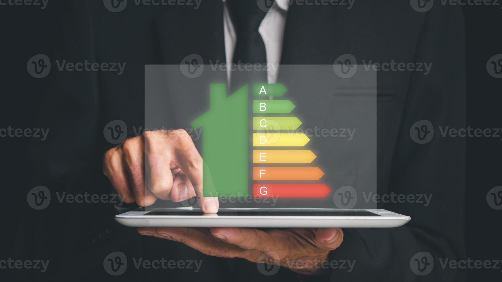 Person hand using digital tablet with house icon energy efficiency scale image on dark background, Concept of ecological and bio energetic house. Energy class. photo
