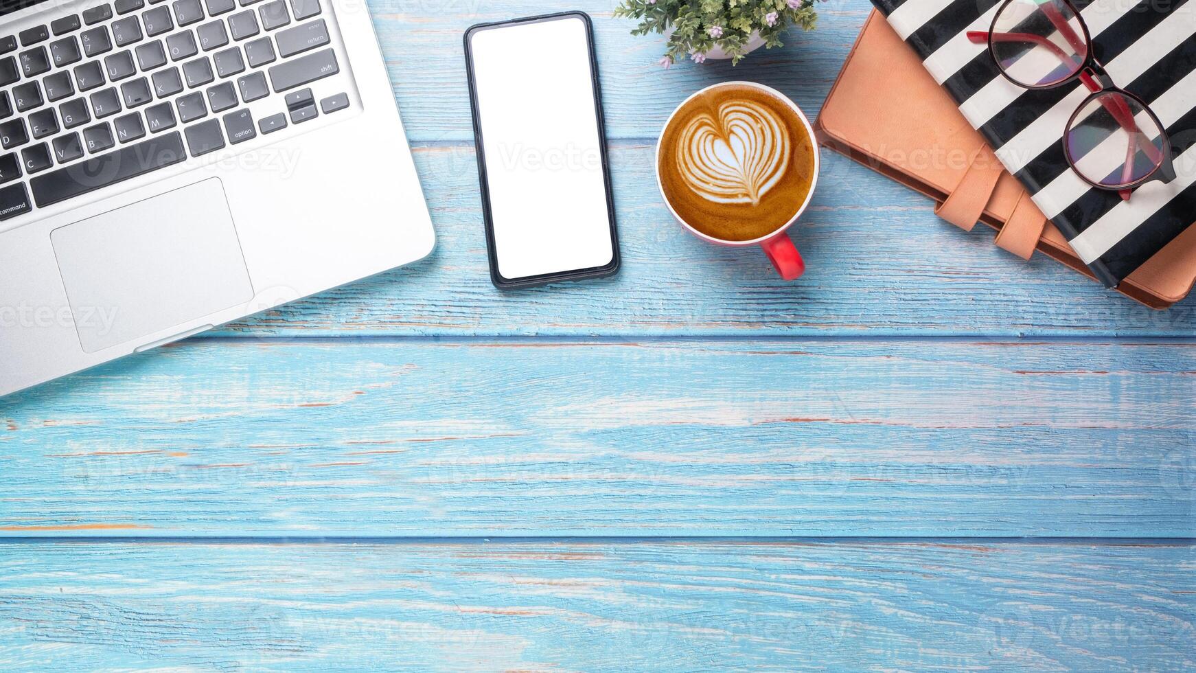 Smartphone with blank screen, laptop, notebook, eyeglass and cup of coffee on wooden desk, Top view flat lay with copy space. photo