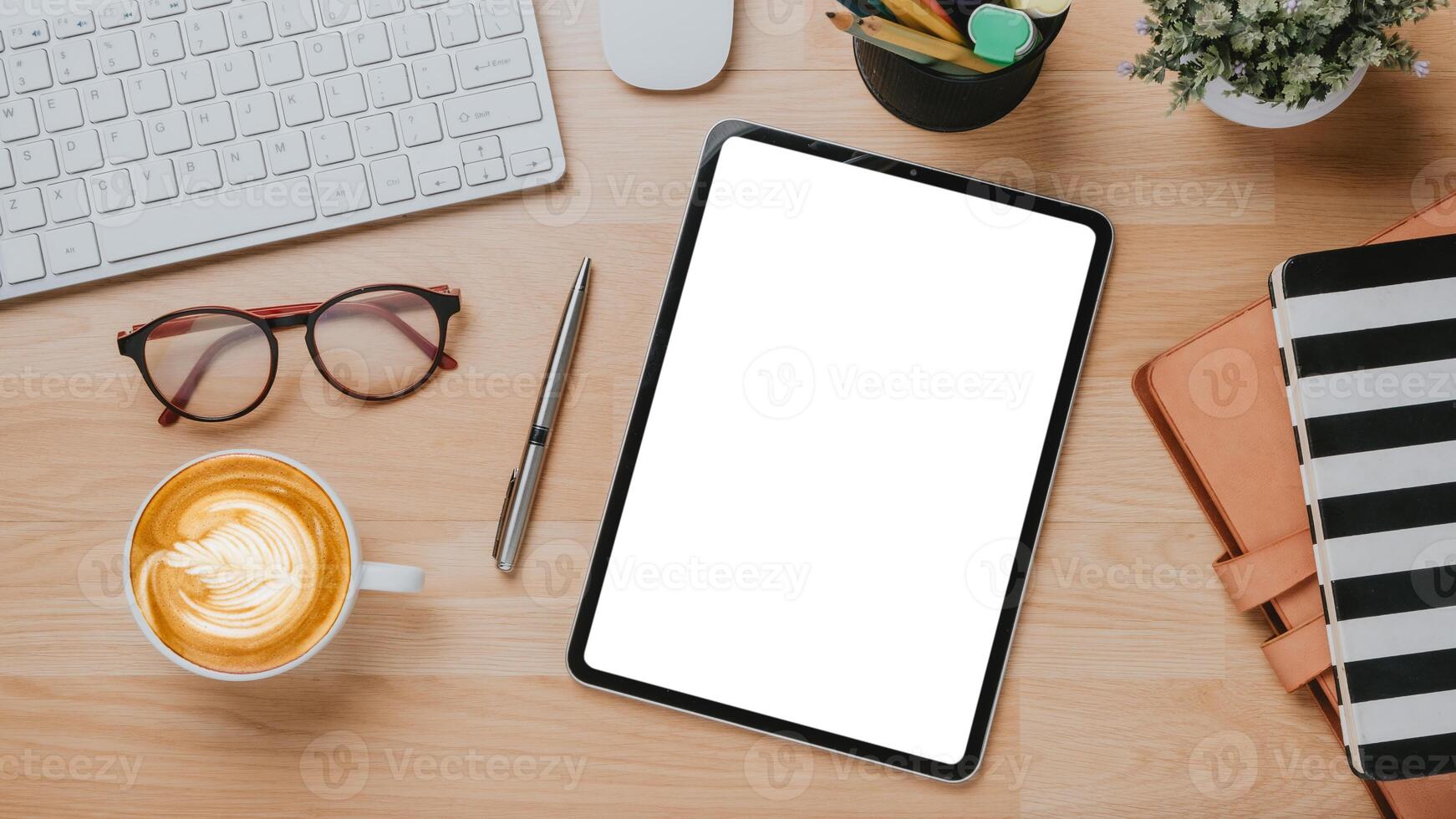 Office wooden desk workplace with blank screen tablet, keyboard, mouse, eyeglass,pen, notebook and cup of coffee, Top view flat lay. photo