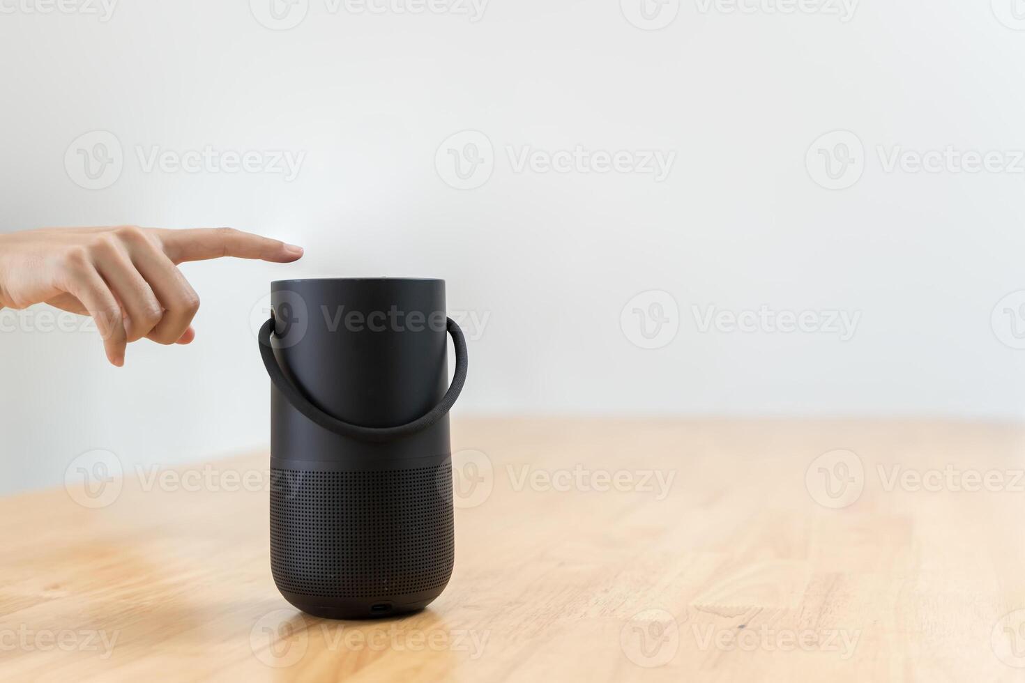 Close-up of hand pressing a button on a wireless Bluetooth speaker surrounded by blurred background. photo