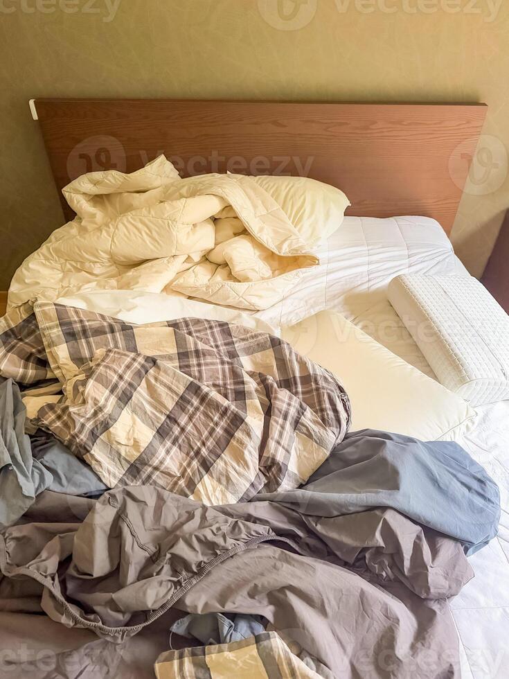 Unmade bed with crumpled sheets, blanket, and pillows, messy bedroom interior. High quality photo