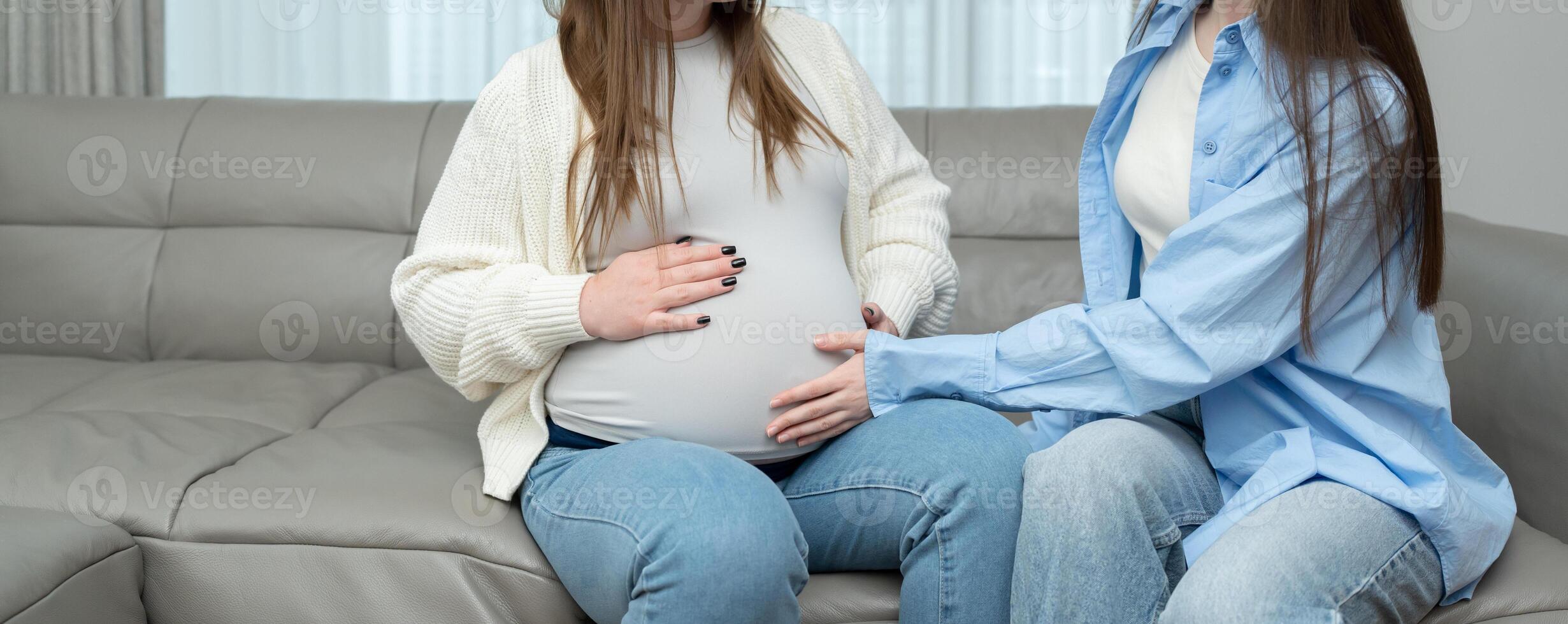 Banner of pregnant woman in third trimester sitting on sofa while her female friend touches her belly with care. Concept of maternity, friendship, connection, support and emotional bonding. photo
