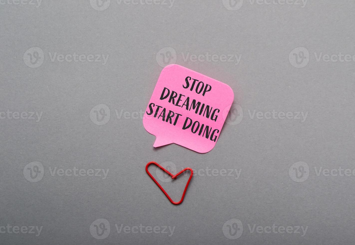 A pink note with the words Stop dreaming start doing written on it photo