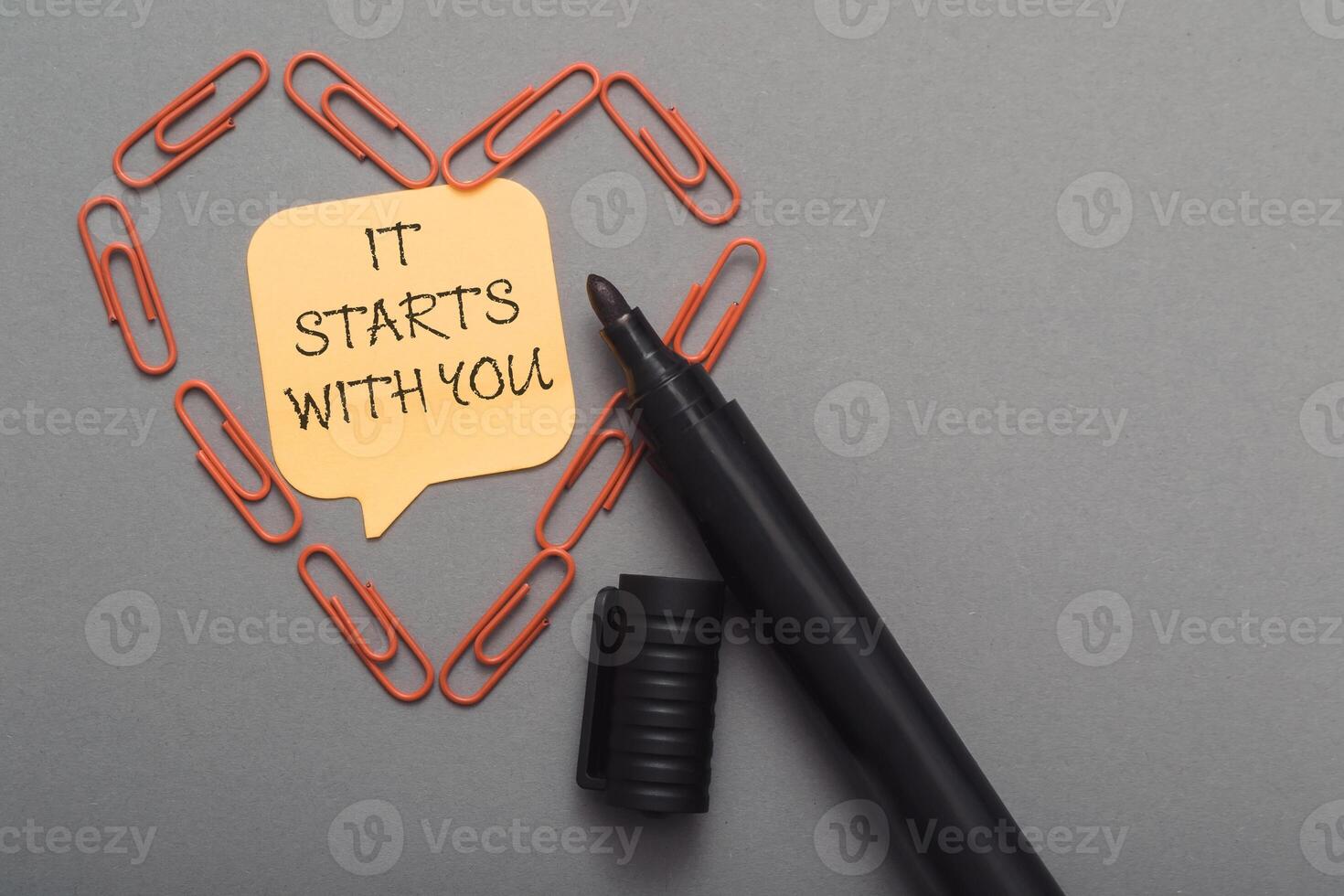 A black pen with a yellow note on it that says It starts with you. photo