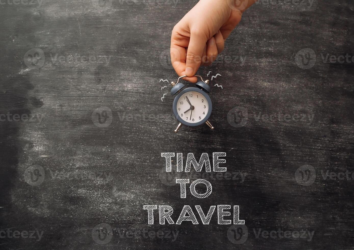 A hand holding an alarm clock with the words Time to travel written below it photo