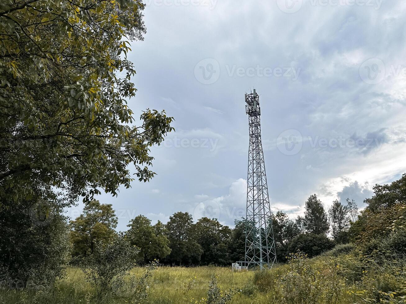 Tall tower is in the middle of a field with trees in the background photo