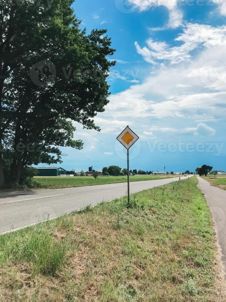 A yellow and white sign is on the side of a road photo